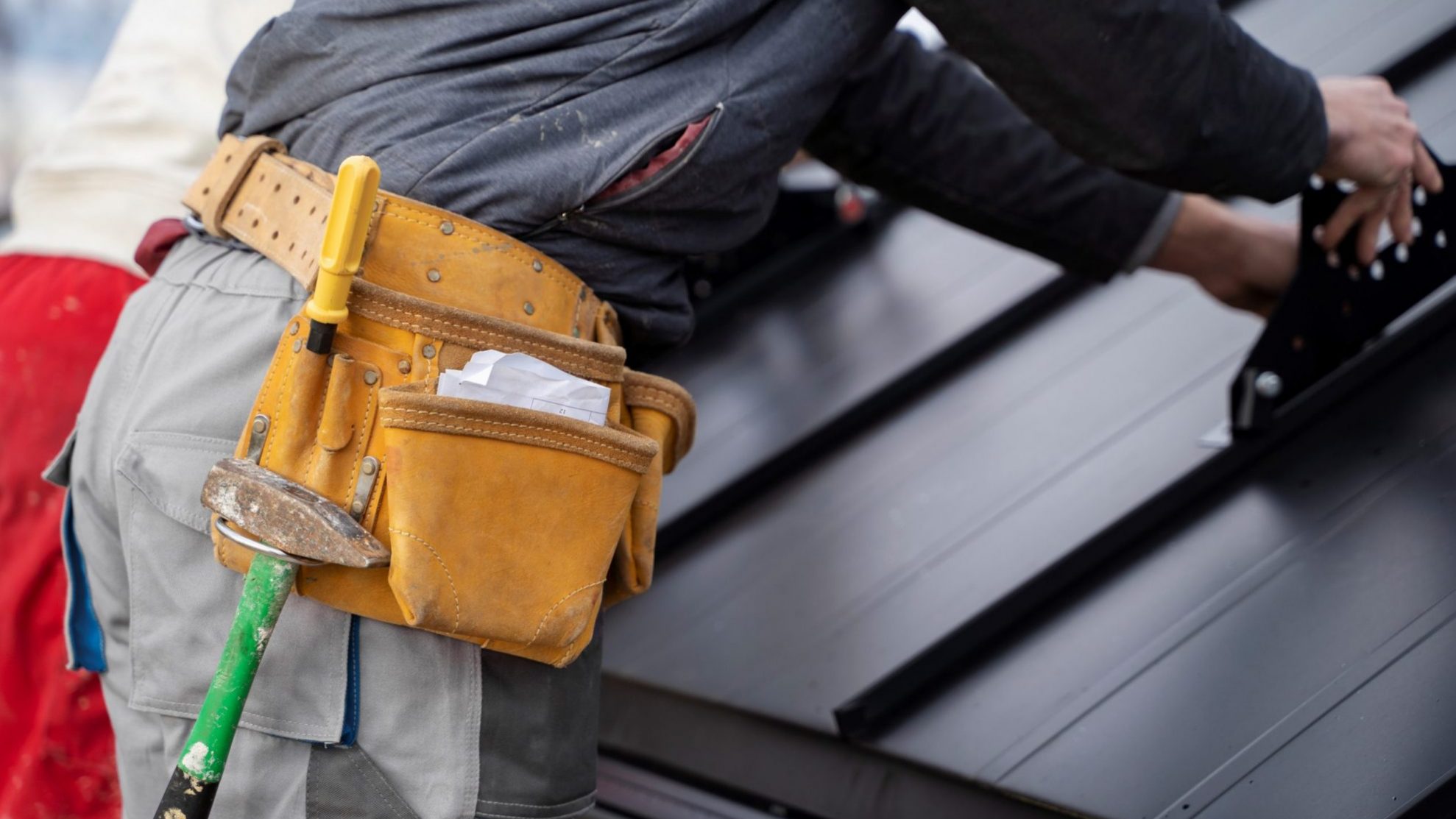 Closeup of man with tool belt repairing roof illustrates blog "Signs That Your Roof Needs to Be Repaired"