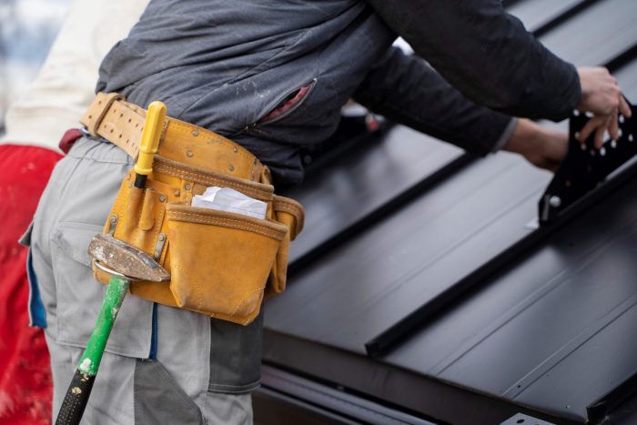 repair-roof-FP Closeup of man with tool belt repairing roof illustrates blog "Signs That Your Roof Needs to Be Repaired"