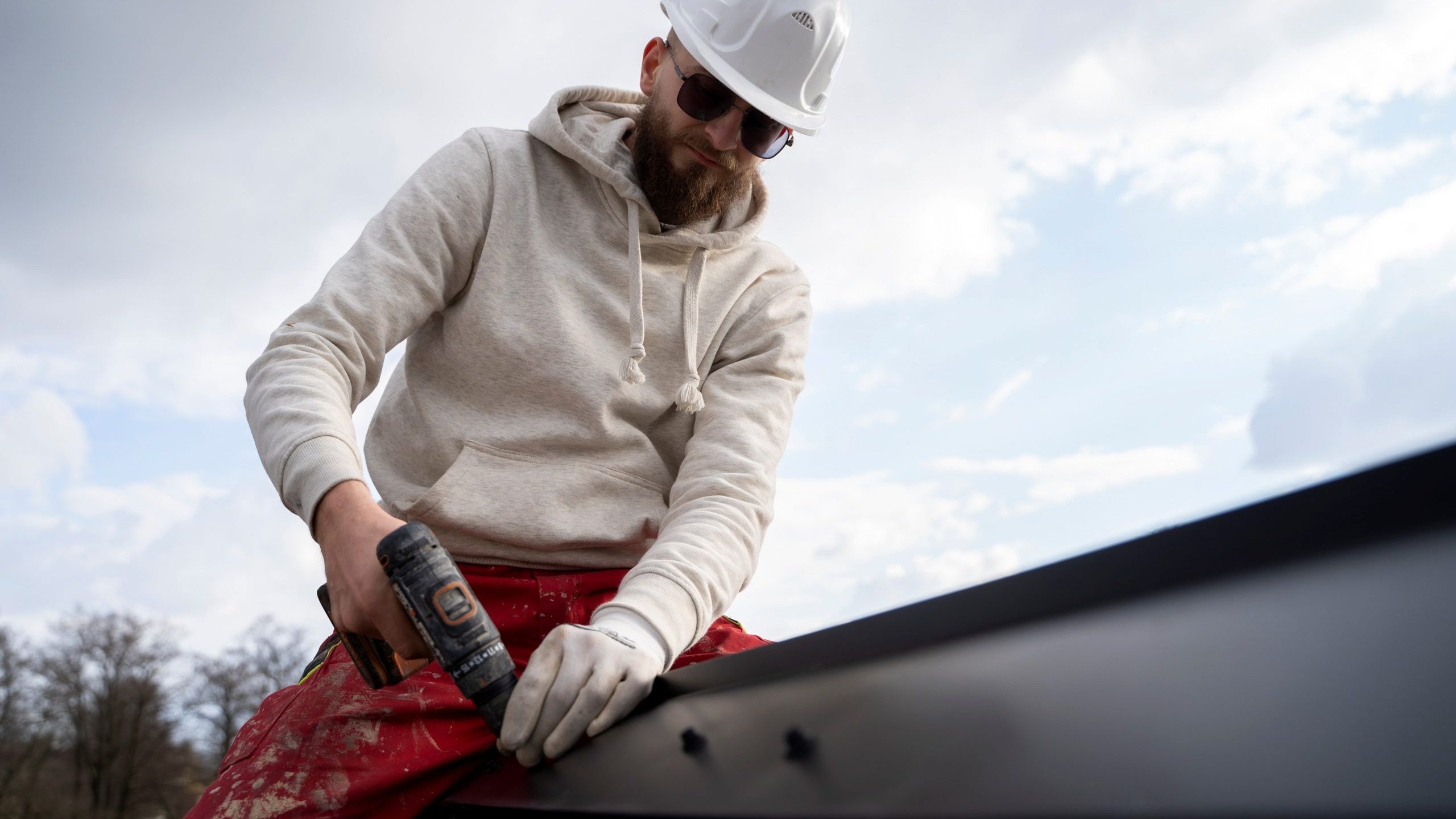 Man wearing hardhat holding drill and fixing roof illustrates blog "Tips To Extend the Lifespan of Your Commercial Roof"