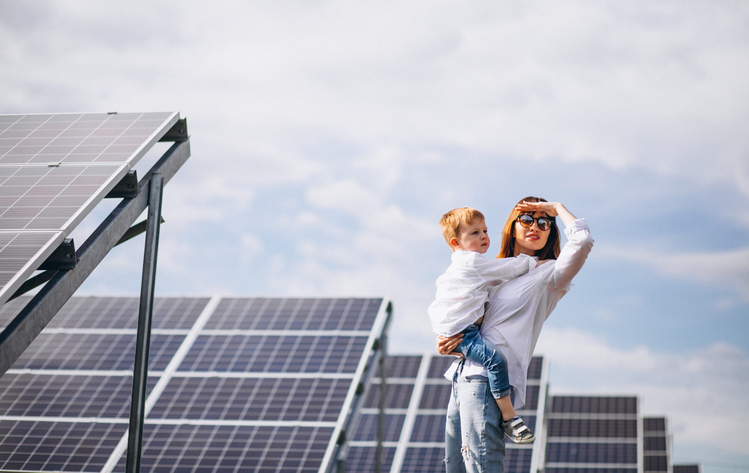 Woman holding child with solar panels in the background illustrates blog "How Do Solar Roof Panels Work?"